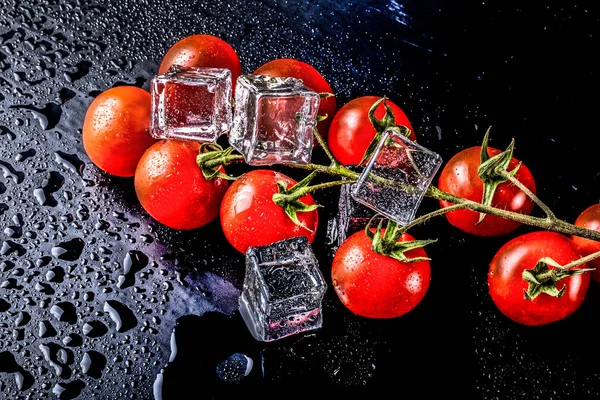 Banch av röda körsbär tomater och isbitar på svart våt bord. Se — Stockfoto