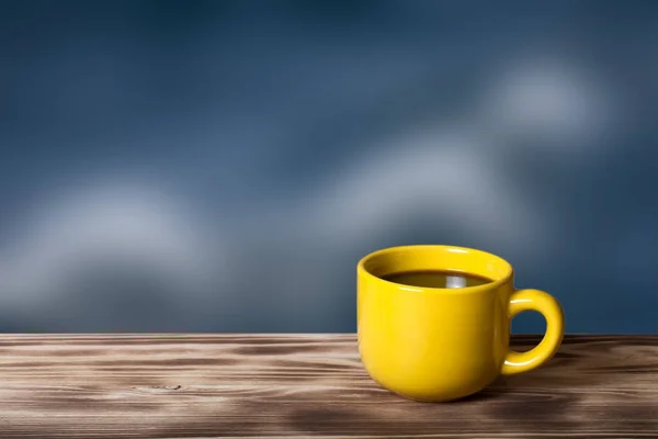 Káva nebo čaj v žluté cup na dřevěném stolu naproti blured — Stock fotografie
