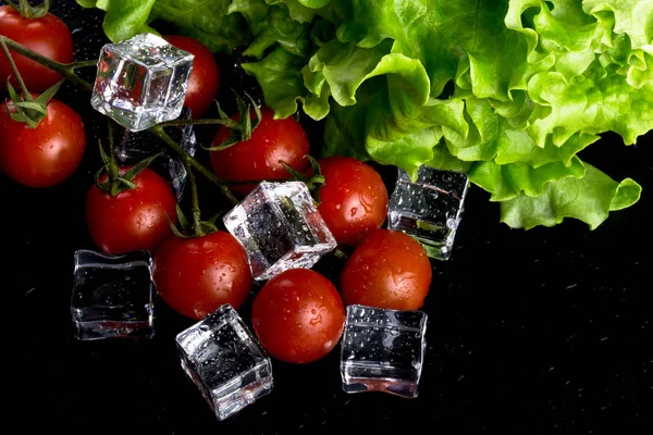 Banch červené cherry rajčat, zelený salát a kostky ledu na černém pozadí — Stock fotografie