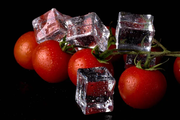 Banch de tomates rojos cereza y cubitos de hielo en la mesa húmeda negro. Se — Foto de Stock