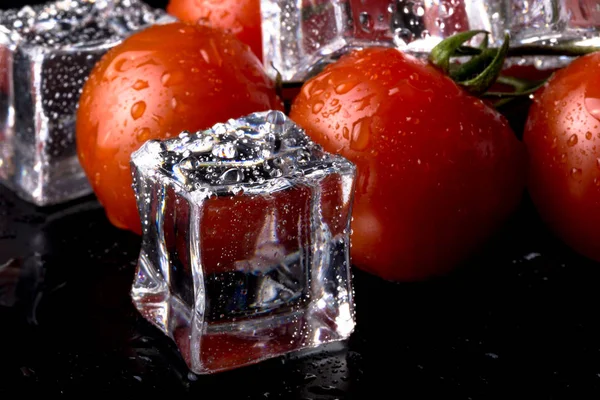 Banch of red cherry tomatos and ice cubes on black wet table. Se — Stock Photo, Image