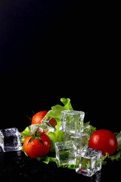 Banch av röda körsbär tomater, grön sallad och isbitar på svart — Stockfoto