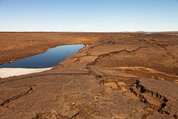 Pequeño lago frío en una tierra seca agrietada en una tranquila primavera desierta — Foto de Stock