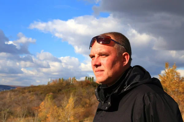 A 35-40-year-old tourist in a black jacket and sunglasses looks thoughtfully into the distance against the background of the landscape.