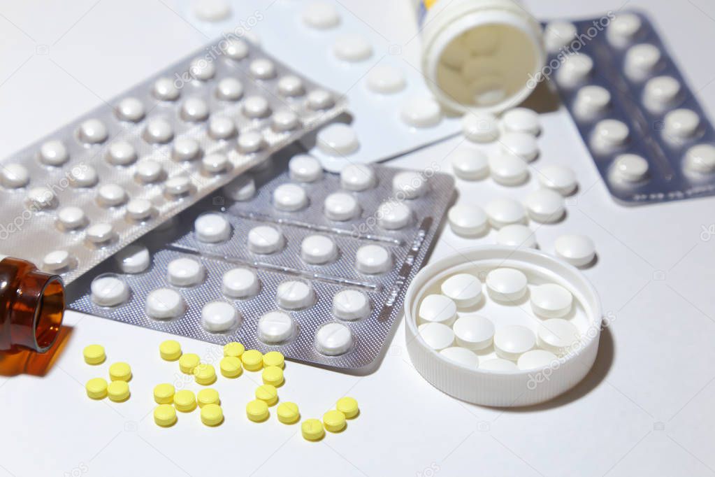 Various tablets - analgesics, antidepressants, vitamins, antiviral drugs scattered on a white background.