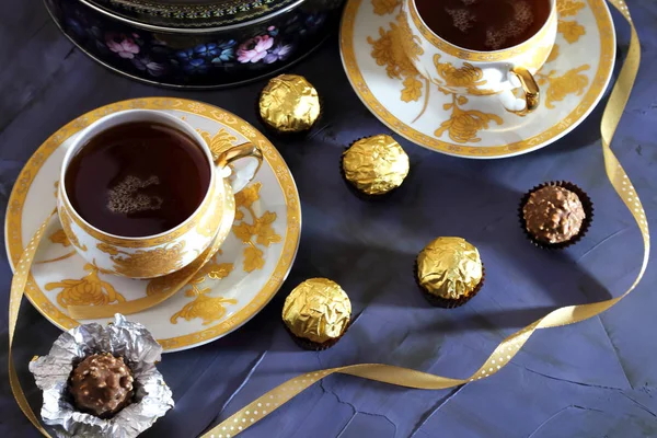 Podczas ceremonii parzenia herbaty. Dwie filiżanki herbaty kolor złoty z czarnej herbaty, pole cukierki, czekolada, ciasteczka na tle BlackBerry. — Zdjęcie stockowe