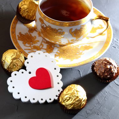 Sevgililer günü, aşk bir sembolü. Natürmort - çay Altın Kupa, hassas kırmızı ve beyaz kalp ve bir siyah çikolata tatlılar dokulu arka plan.