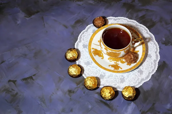 Evening tea party. Porcelain golden cup with tea and dessert chocolate candy.