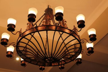 Bir büyük antik vintage yuvarlak metal avize dekoratif elemanları ile bronz renk altın arka plan tavanda yanan lambalar ile asılı..