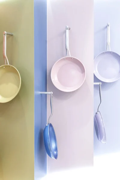 Colored new clean multi-colored pans hang on a store showcase. Kitchen utensils, metal kitchenware for cooking, household goods bright yellow purple green pink blue pastel colors — Stock Photo, Image