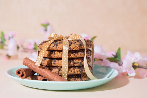 Frisch gebackene Haferflockenplätzchen auf einem blauen Teller vor Pfirsichhintergrund und einem Zweig eines blühenden Apfelbaums. leckeres gesundes, süßes kulinarisches Dessert für ein romantisches festliches Frühstück, Essen — Stockfoto