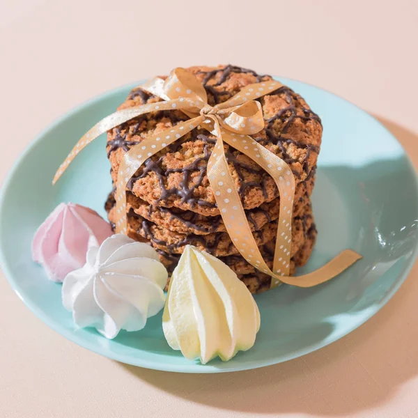 Frisch gebackene Haferflocken knusprige Kekse auf einem blauen Teller auf einem pfirsichfarbenen Hintergrund und schöne französische mehrfarbige Baiser. leckeres kulinarisches Dessert, romantisches Festfrühstück, Essen, Snacks — Stockfoto