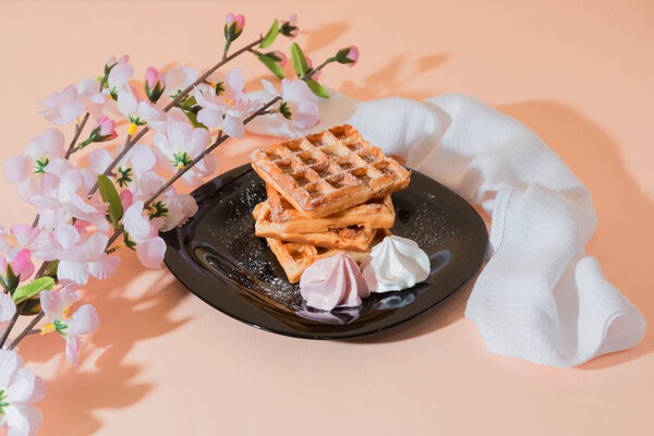 Sweet delicious dessert, homemade baked goods for breakfast. Belgian European soft waffles on a black plate and meringue
