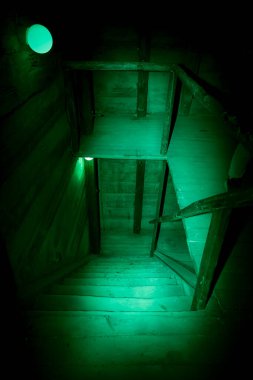 Cadılar bayramının gizemli, korkunç tavan arası. Gizemli paranormal bir bodrumda ya da tavan arasında, lambanın yeşil ışığında siyah gölgesi olan eski, kirli, ahşap merdivenler.