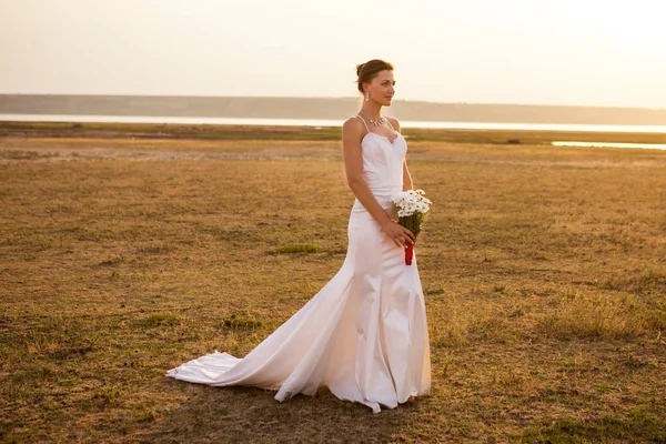 Beautiful bride with a bouquet of chamomiles standing in the fie — Stock Photo, Image