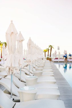 Beyaz şemsiye ve şezlong-lonque günbatımı zamanı yüzme havuzunda yakınındaki