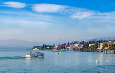 Powerboat yelken Garda Gölü, İtalya. Göl Manzaralı tekne ve Sirmione binalar ile. Güzel manzara mavi su, temiz gökyüzü bulutlar ve arka plan üzerinde dağ ile.