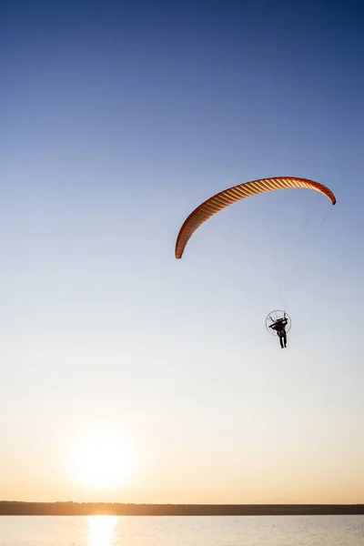 Paraglider fly, sunset time. The sportsman flying on a paraglider orange color near the sea.