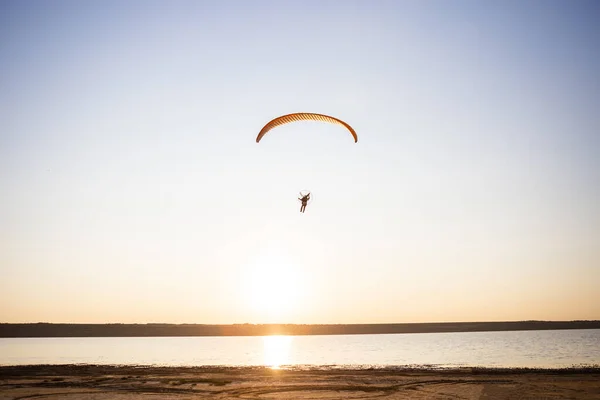 Paraglider fly, sunset time. The sportsman flying on a paraglider orange color near the sea.