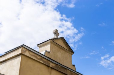 Taştan haçı olan eski bir kilise çatısı, arkasında bulutlu bir gökyüzü. Dinlenme, ibadet, Hıristiyan sembolü kavramı.