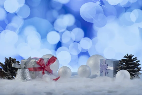 Composición navideña con caja regalo o regalo, conos de pino y bolas de nieve decorativas contra fondo de luces navideñas — Foto de Stock