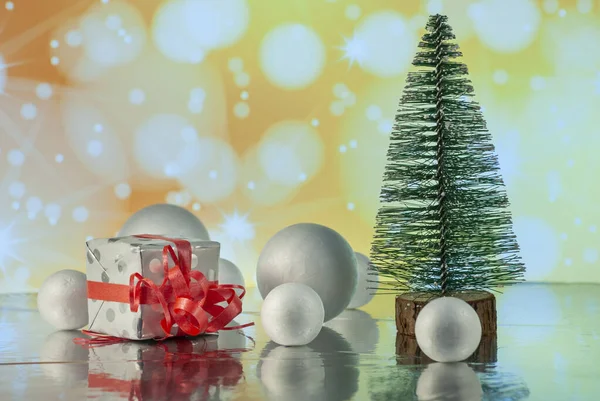 Composición navideña con árbol de Navidad, caja de regalo o regalo y bolas de nieve decorativas contra luces navideñas — Foto de Stock