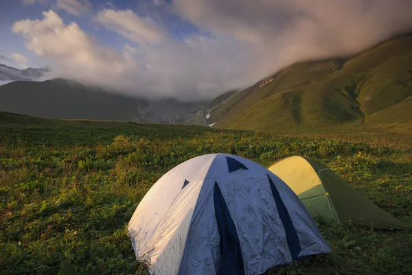 Camping tents on grassy hill in the misty mountains