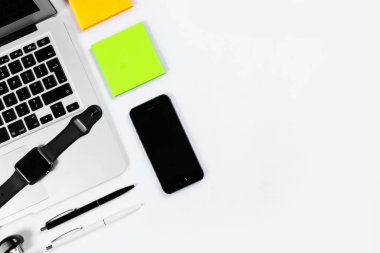 Çalışma masa üstü görünümü, düz yatıyordu. İş öğeleri beyaz bir tablo, dizüstü bilgisayar, saat, telefon, kalemler, çıkartmalar. Kopya alanı, iş öznitelikleri kavramı.