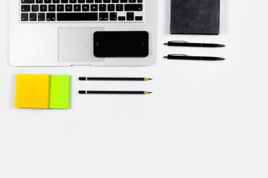 Çalışma masa üstü görünümü, düz yatıyordu. İş öğeleri beyaz bir tablo, laptop, kalemler, çıkartmalar. Kopya alanı, iş öznitelikleri kavramı.