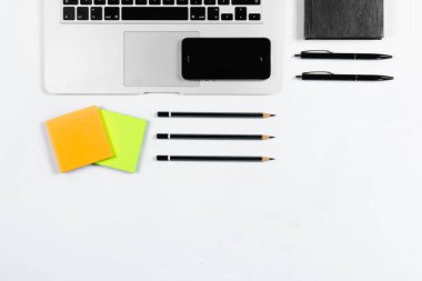 Çalışma masa üstü görünümü, düz yatıyordu. İş öğeleri beyaz bir tablo, laptop, kalemler, çıkartmalar. Kopya alanı, iş öznitelikleri kavramı.