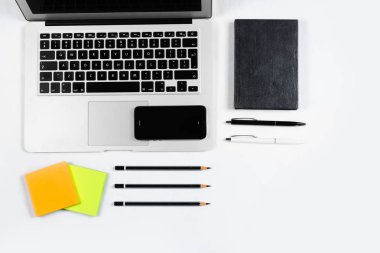 Çalışma masa üstü görünümü, düz yatıyordu. İş öğeleri beyaz bir tablo, laptop, kalemler, çıkartmalar. Kopya alanı, iş öznitelikleri kavramı.