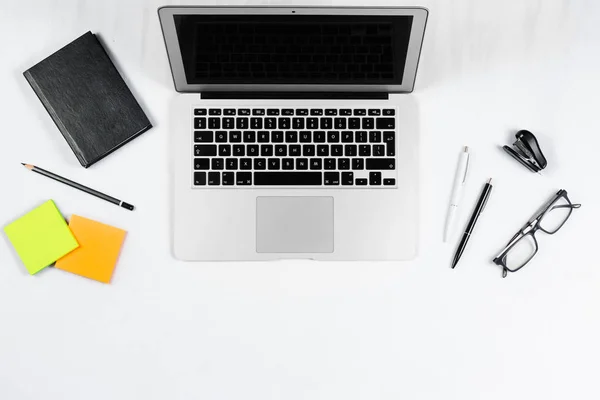 Mesa de trabajo vista superior, plano laico. Artículos de negocios en una mesa blanca, portátil, reloj, teléfono, bolígrafos, pegatinas. Espacio de copia, Concepto de atributos de negocio . — Foto de Stock