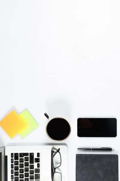 Mesa de trabajo vista superior, plano laico. Artículos de negocios en una mesa blanca, portátil, teléfono, bolígrafos, pegatinas. Espacio de copia, Concepto de atributos de negocio . — Foto de Stock