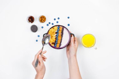 Odaya Servis Kahvaltı, ev yapımı yoğurt ve Mısır gevreği ve taze yaban mersini ile bir kase üzerine bir kaşık tutan eller, bir bardak portakal suyu bir beyaz arka plan, üstten görünüm, düz yatıyordu. Sağlıklı fo kavramı