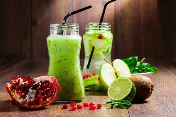 Green cocktail in a glass jar of kiwi, green apple, mint, lime and pomegranate on a wooden brown background. A refreshing drink. The concept of healthy eating, detox.