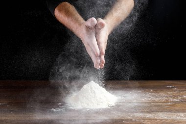 Aşçı yakın çekim el hamur siyah bir arka plan üzerinde pişirmek için masanın üzerine un dökün.