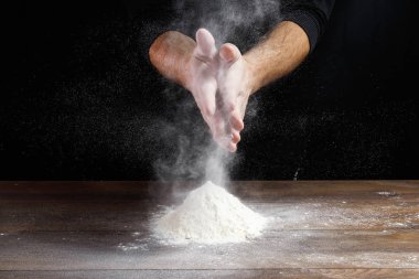 Aşçı yakın çekim el hamur siyah bir arka plan üzerinde pişirmek için masanın üzerine un dökün.