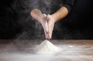 Aşçı yakın çekim el hamur siyah bir arka plan üzerinde pişirmek için masanın üzerine un dökün.