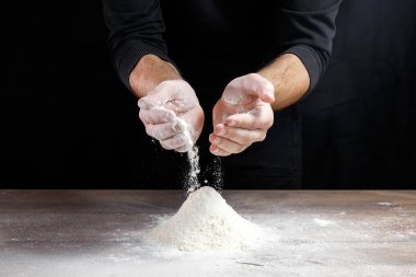 Aşçı yakın çekim el hamur siyah bir arka plan üzerinde pişirmek için masanın üzerine un dökün.