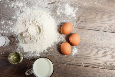 Üstten Görünüm yumurta, un, bir bardak taze süt, hamur ahşap bir masa arka plan üzerinde yemek. Yat, alanı Kopyala.