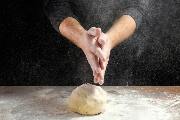 Male hands chef close-up, knead the dough, cook the dough on a dark background.