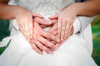 Bir kız bir ipek elbise içinde bir sandalyeye oturur ve ellerini dizlerinin üzerinde haçlar.