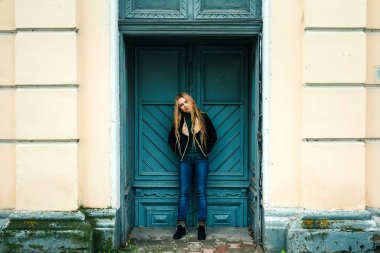 Marihuana yaprağı ağzında tutarak ve eski kapıya yaslanmış retro güneş gözlüğü takıyor şapkalı hippi sarışın kız... Yumuşak ışık, sokak stili.