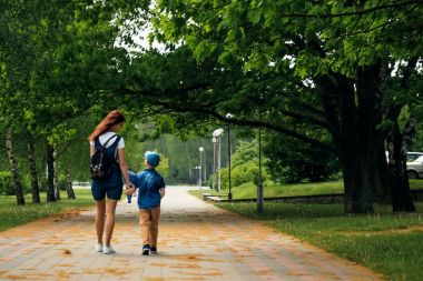 Genç bir anne ve oğlu güzel yaz park boyunca yürüyor. Bir çocuk ve güzel bir kadın yürüyüş ve eğleniyor. Aile portre açık havada.