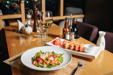 Salata karides, avokado, domates, marul ve limon. Beyaz bir tabak, restoranda bir tablo. Suşi susam Maki.