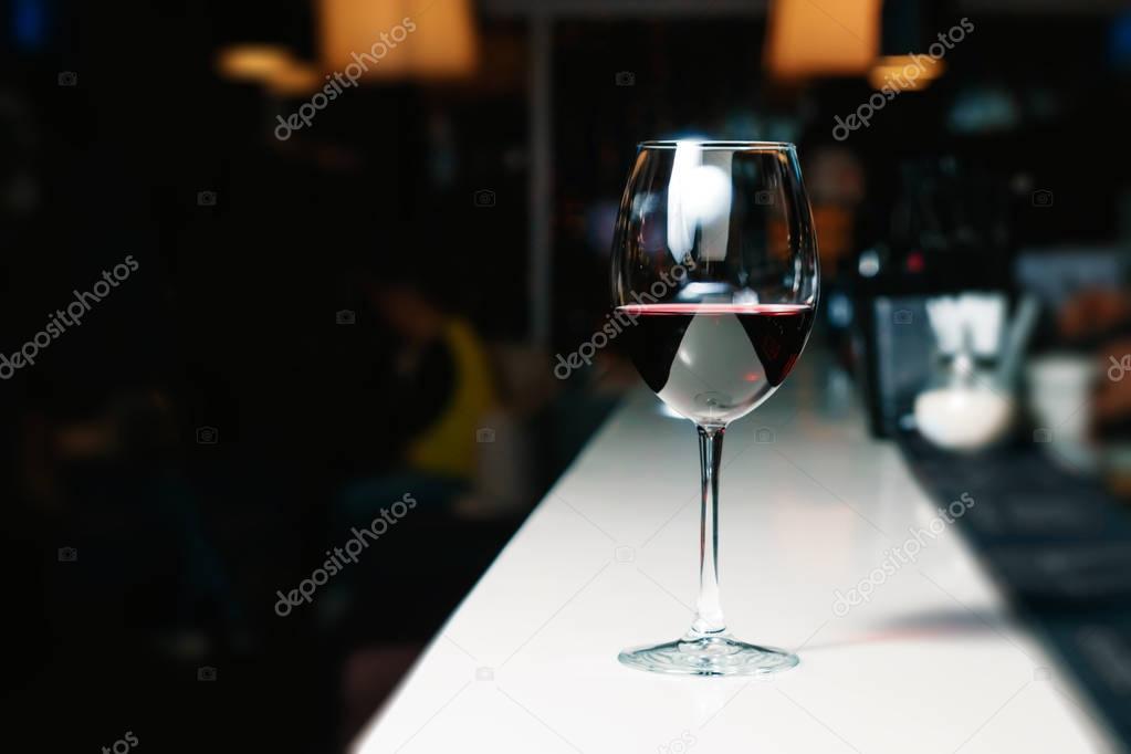 A glass of red wine close-up on a bar, white counter. Dark background.