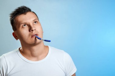 Bir adam beyaz tişört, mavi bir arka plan karşı dişlerini fırçalayıp fırçalamadığını. Ağız hijyeni kavramı.