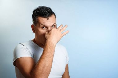 Yakın çekim portre bir adamın burnunu elleriyle kapatır. Hafif bir arka plan üzerinde. Konsept kötü koku, koku.