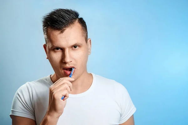 一个穿着白色 T恤衫的男人把牙齿刷在蓝色的背景上 口腔卫生的概念 — 图库照片