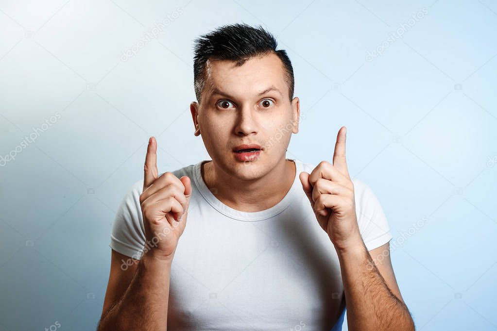 Portrait of an emotional white man, depicted on a blue background, looking at the camera with round eyes and a raised index finger, as if he had found a solution to the problem, the idea came.